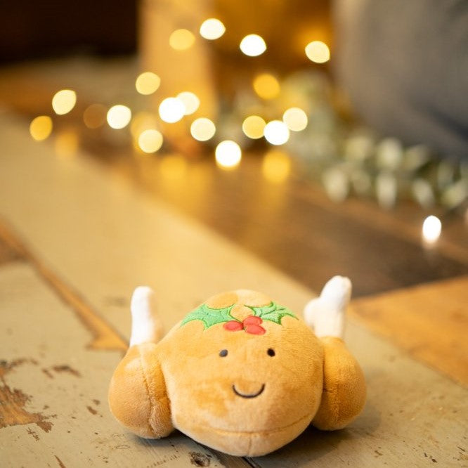 Plush dog toy resembling a roast turkey on a wooden surface with lights in the background