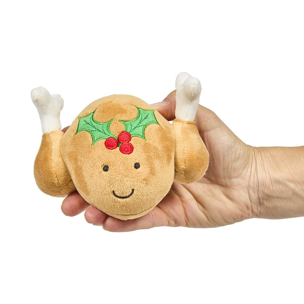 Plush toy resembling a roasted turkey with a face and holly decoration held in a hand 
